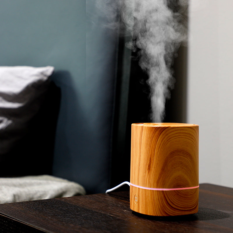 Sand wood grain aroma diffuser releasing mist on a dark side table
